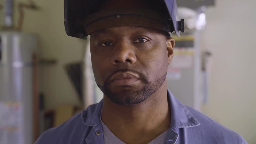 A worker wearing a black soldering hat looking at the camera inside a factory