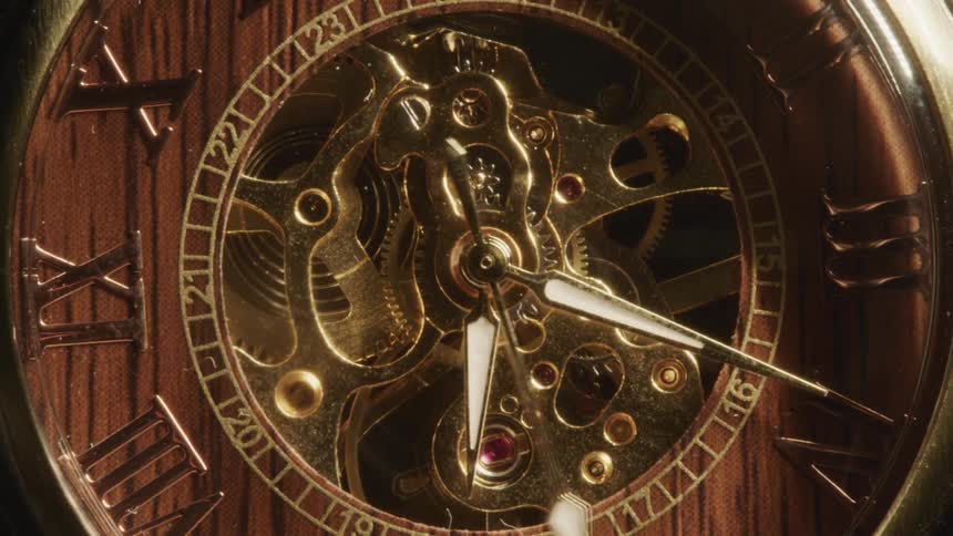 A golden mechanical clock watch lays flat as one of its arms rotates swiftly around its face