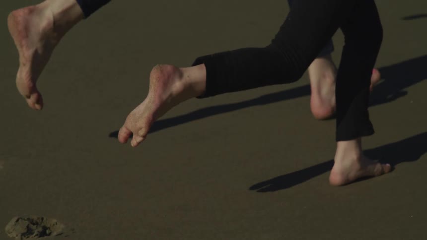 Mother and daughter holding hands running barefoot on the beach