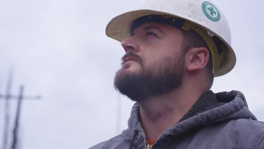 A man in a hard hat looks up at sky contemplatively on a cloudy day