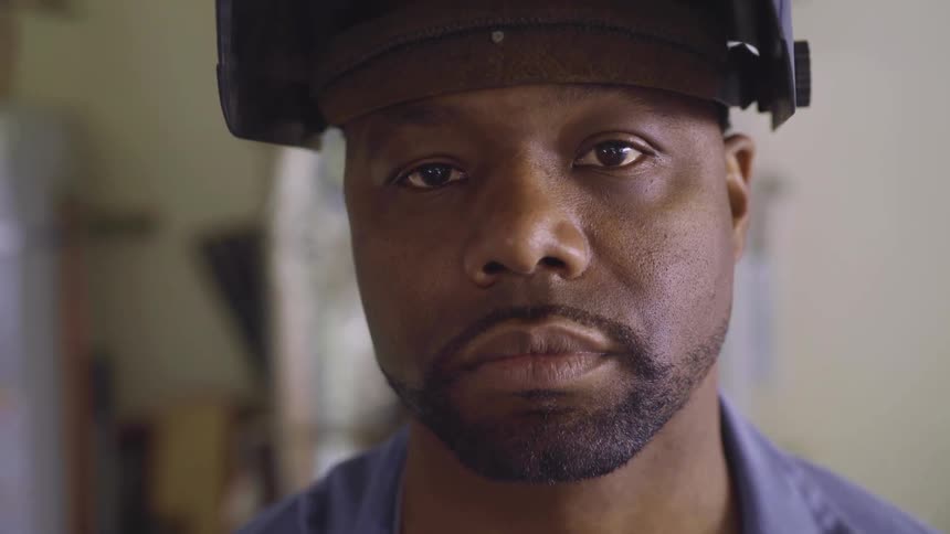 A man wearing a black soldering mask looking at the camera inside a factory