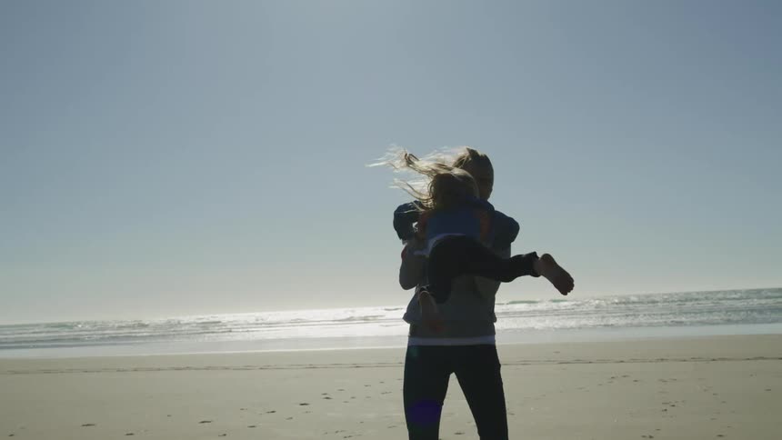 A woman plays with a child and swings her around on a beach