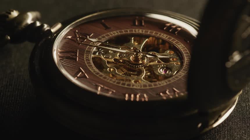 A golden mechanical pocket watch lays flat as its arms rotate around its face