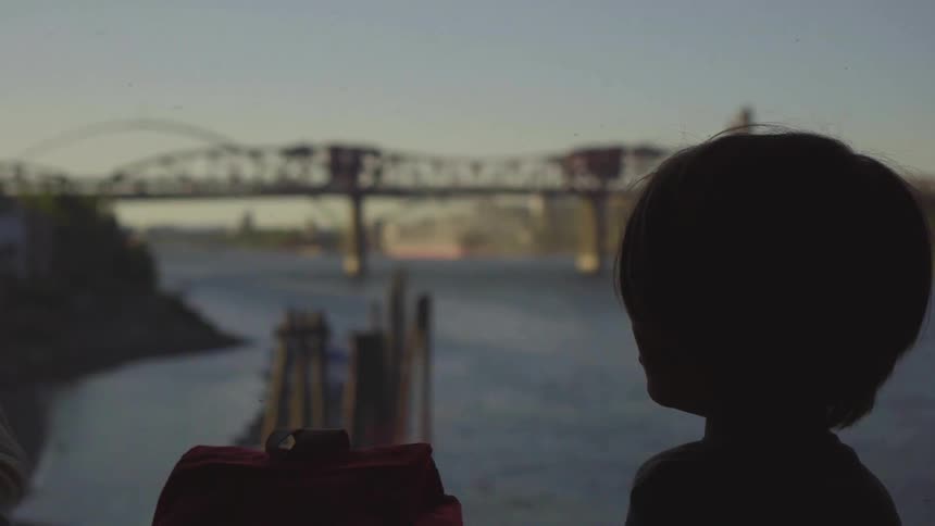 Infant looking out the window of a train while crossing on a bridge over a river at evening