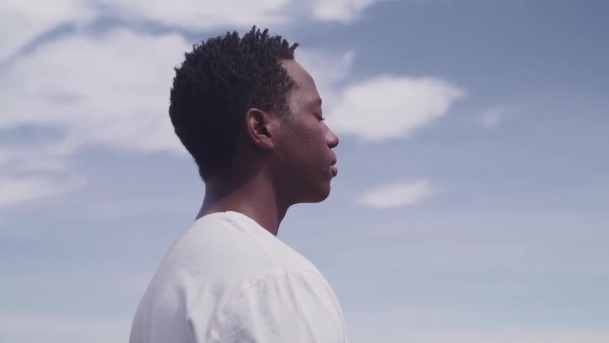 A man is standing outside with his eyes closed