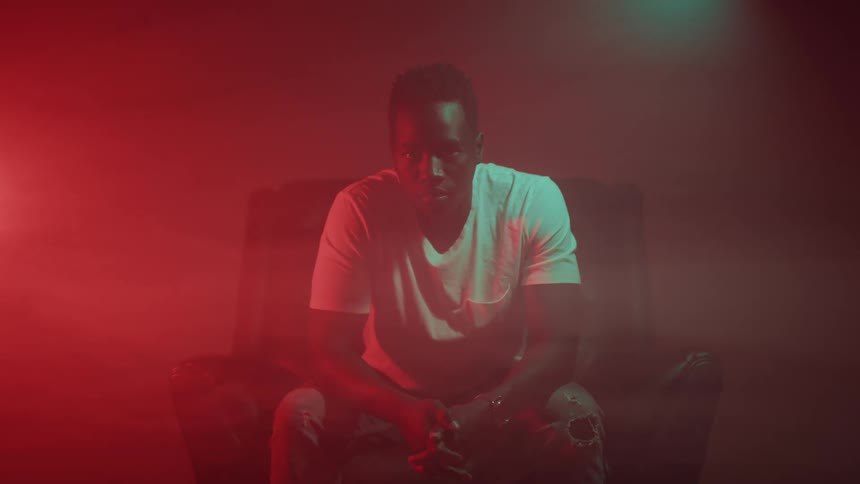 A young man sits in a chair in a smoky room