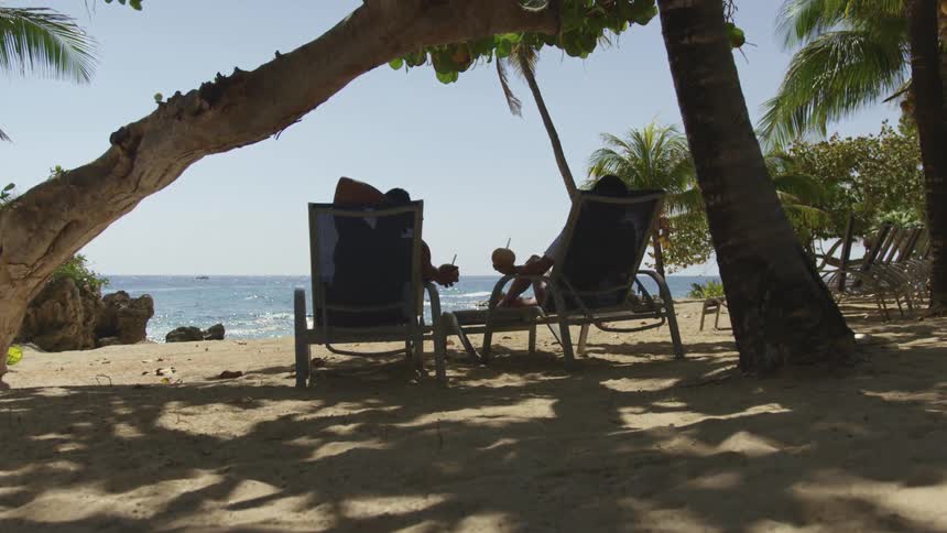 Two people sit in beach chairs on a sandy quiet beach by the ocean
