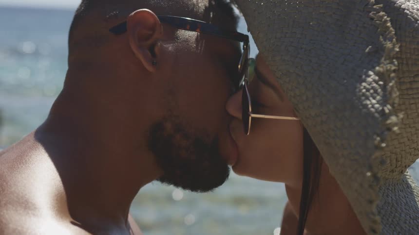 A male and female couple kiss romantically while outdoors at a sunny beach