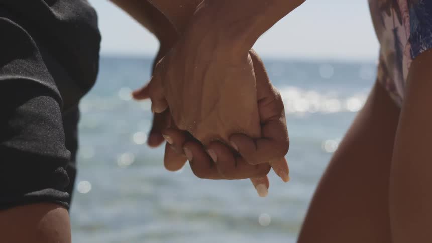 A man and woman hold hands while standing at the coast overlooking the ocean