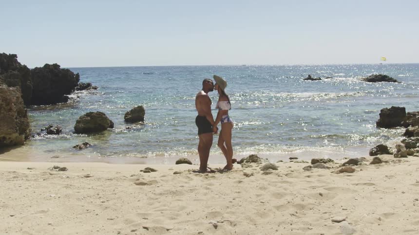 Couple kissing on sandy shoreline near rocks at the beach
