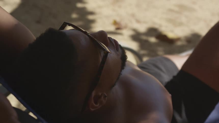 A man is leaned back relaxing outdoors with sunglasses on