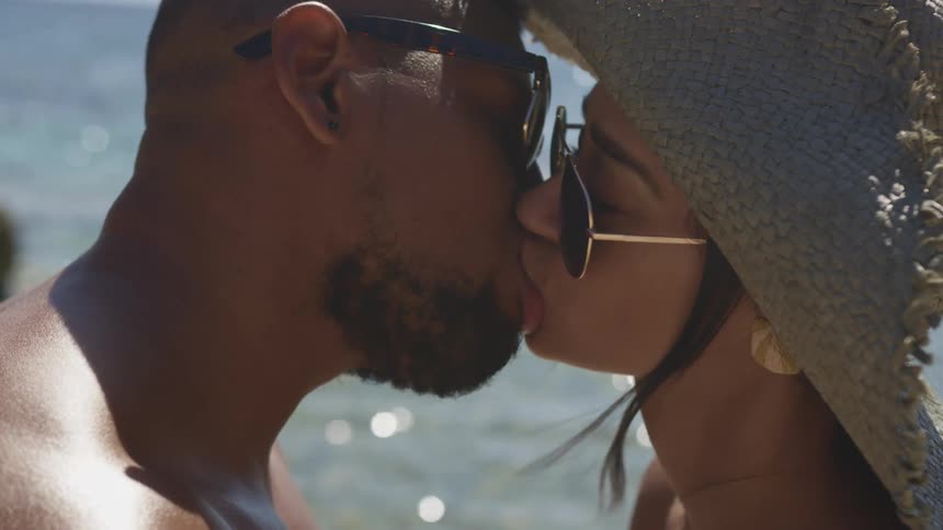 Young couple wearing sunglasses kissing on a tropical beach