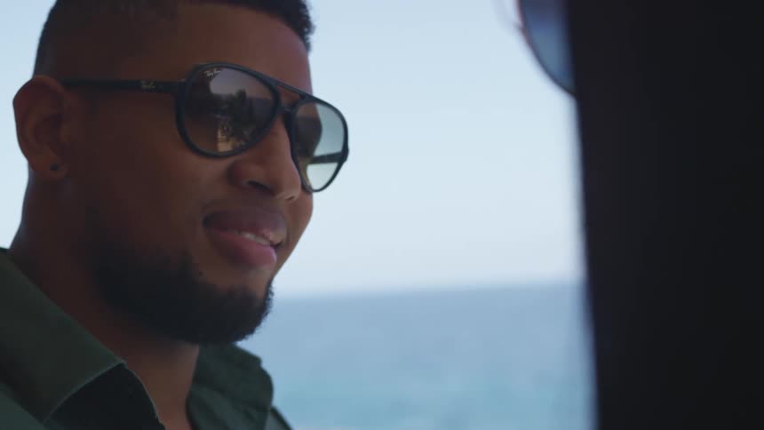 Man wearing glasses smiles while looking at a woman standing near the ocean