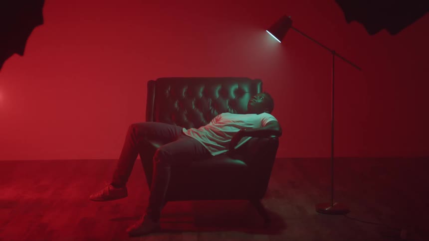 Young man sprawled on a couch under a lamp inside a red room