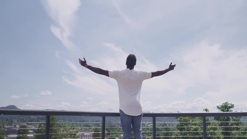 Young man standing on a porch open his arms to the blue sky