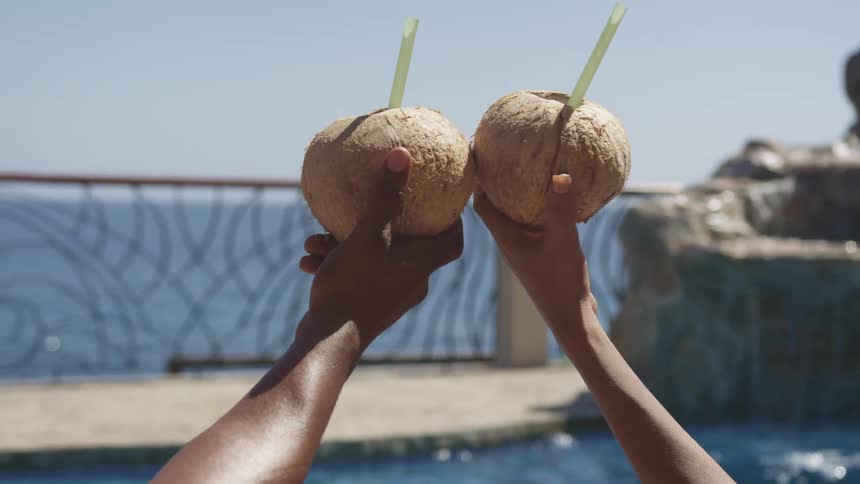 Young couple toasting with coconut shell cocktails in a pool on a tropical beach