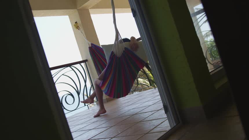 A person leisurely relaxing on a hammock hanged on the porch of a tropical house