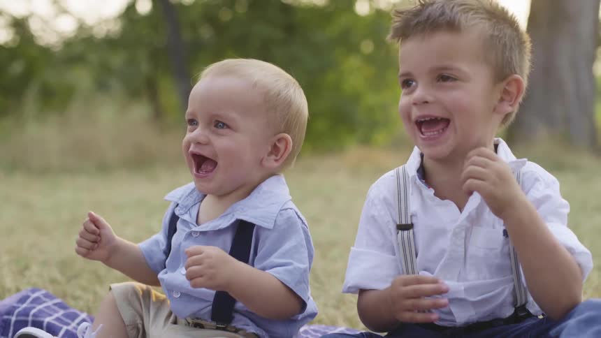 Two little boys sit outside on grass laughing