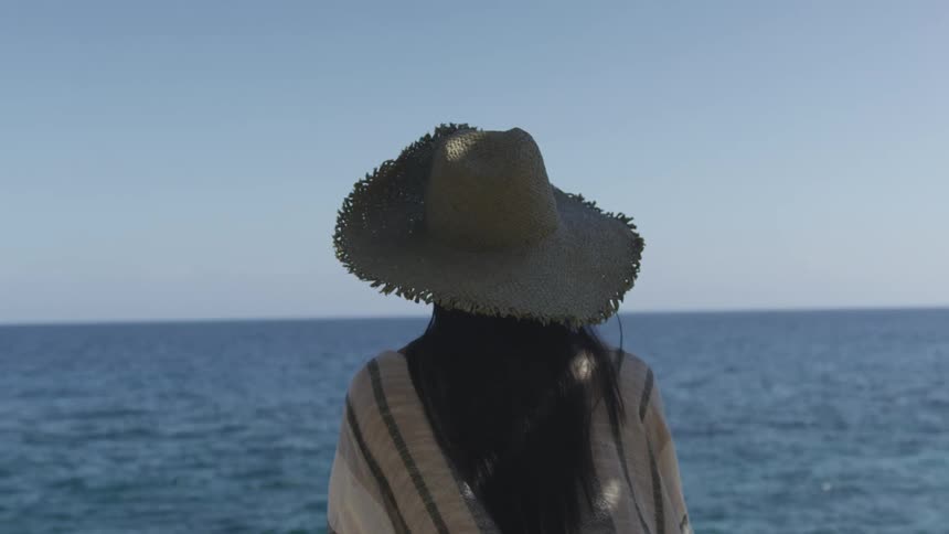 Young woman wearing a sun hat looking at the ocean in the carribean
