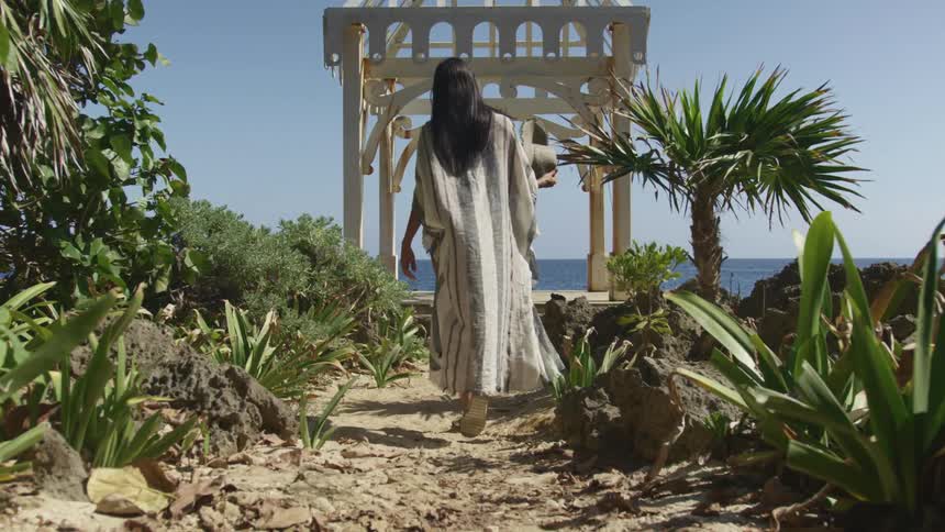 A woman is walking on sand toward a gazebo