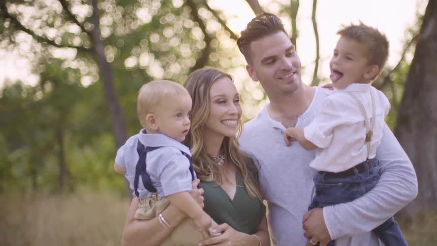 Young couple with kids modeling and smiling for a photo outdoors at sunset
