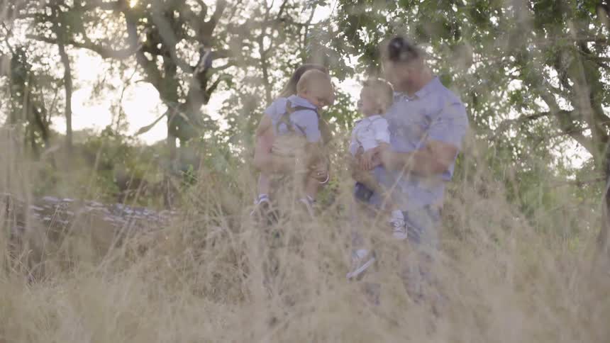 Family of four standing on a field behind the tall dry grass at sunset