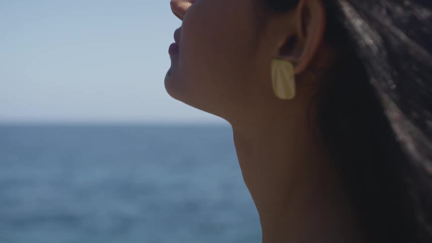 A woman stands near the ocean and lets the wind through her hair