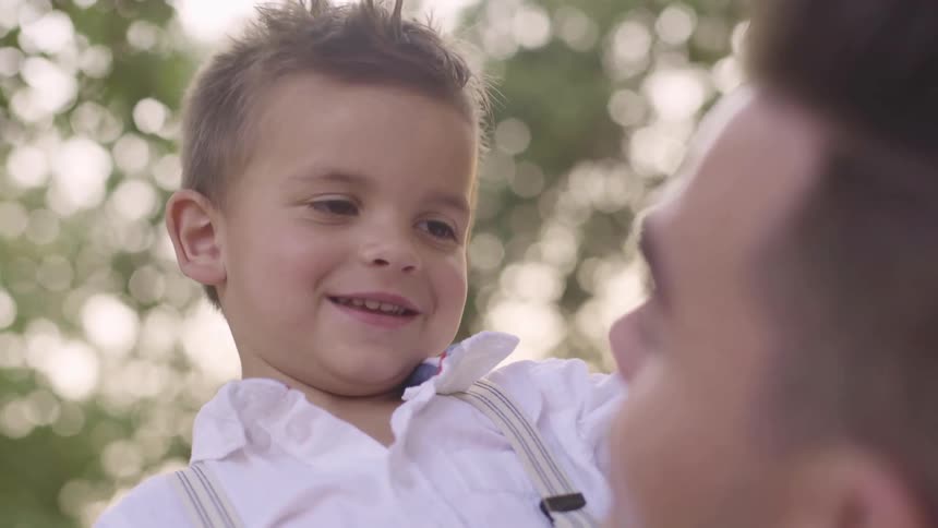 Man holds smiling toddler in his arms under trees