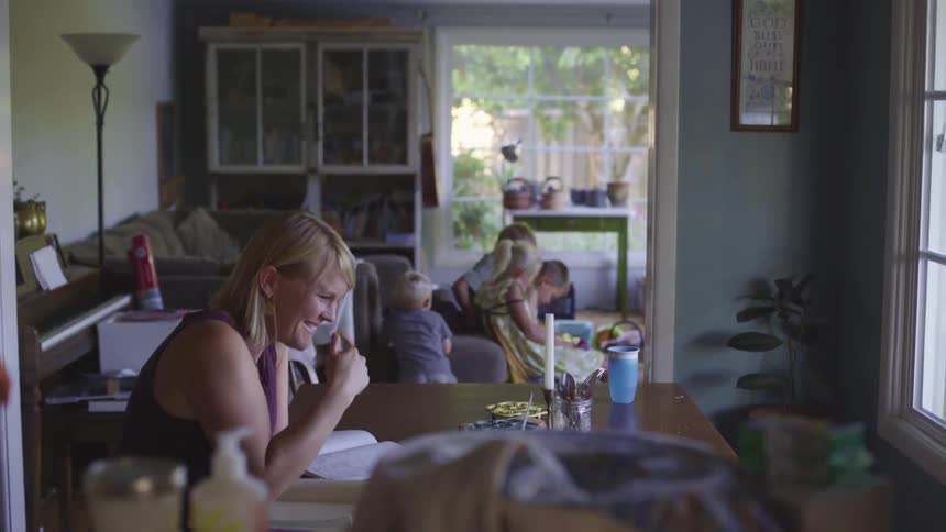 A woman in a room sitting at a table smiling with children in the background