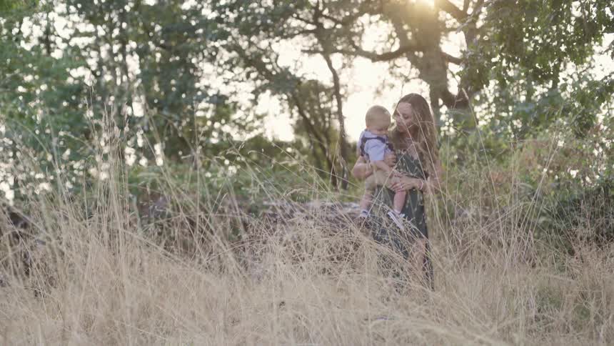 A mother stands in a forest holding her baby son