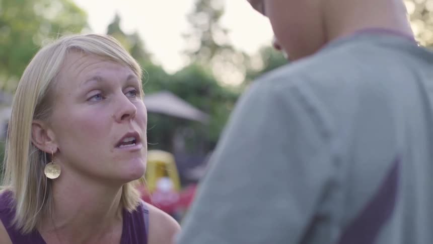 A woman is crouching down and speaking to a male child outdoors