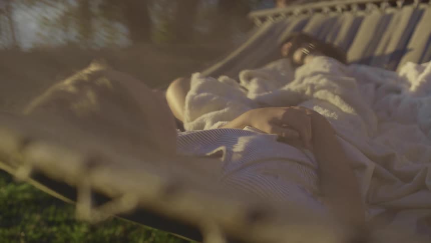 A person lounges on a hammock covered by a white blanket outdoors at dusk