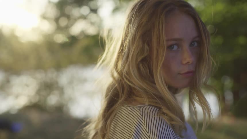 Young blonde woman looking at the camera in the forest near a lake at sunset