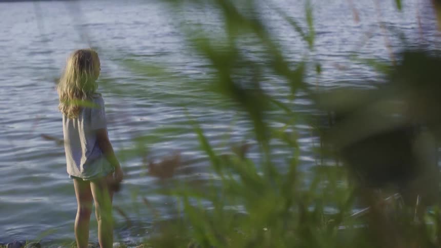 A young girl stands on the shore and looks out at the water