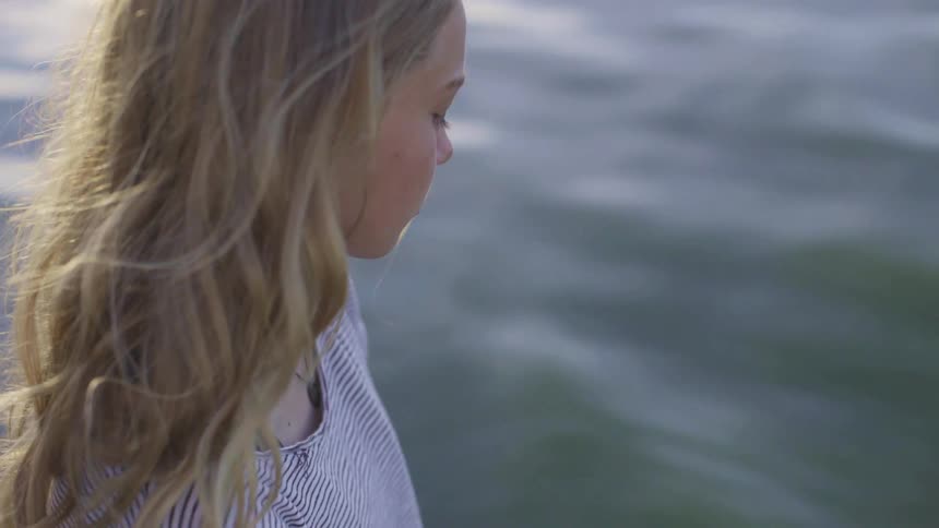 Young blonde woman sanding reflectively near a lake at evening