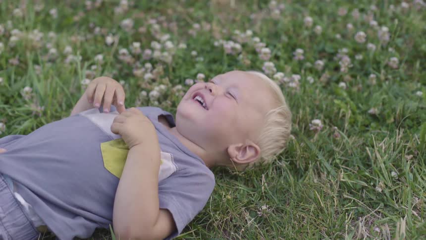 A woman tickles her baby boy who lies in a field with clover and then rolls over