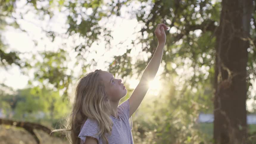 Teen girl playfuly looking up near the trees at sunset