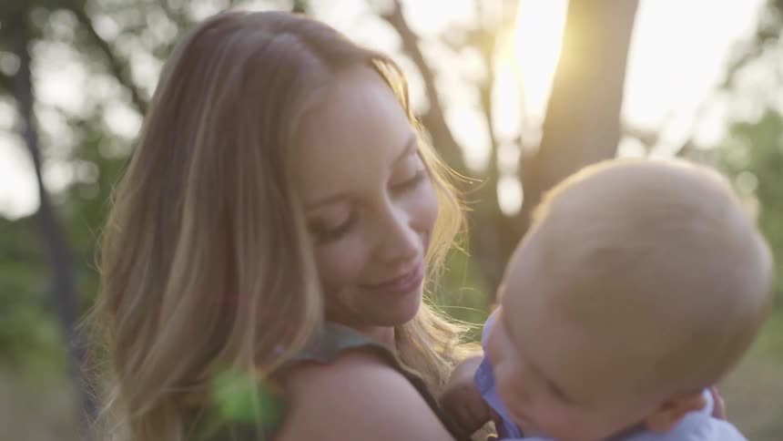 A young woman holds her baby son outside under trees