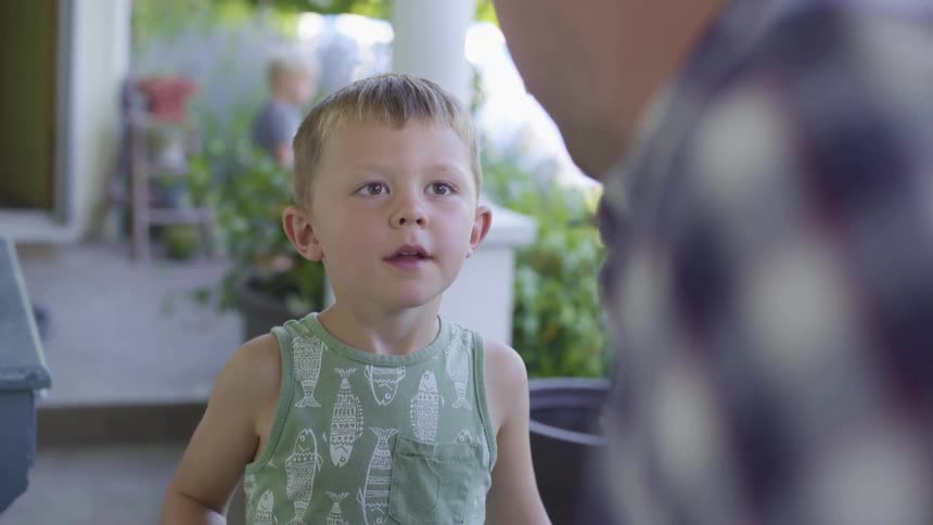 A little boy outside at home looks at his dad