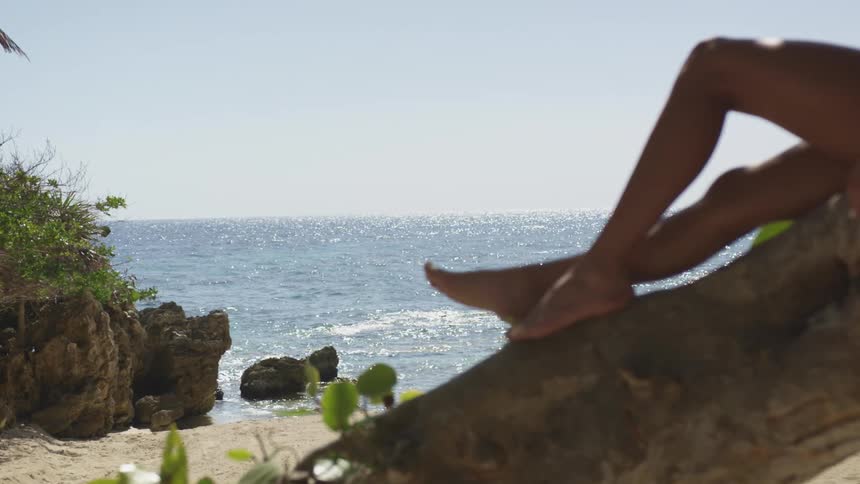 A woman reclines on a tree trunk while relaxing near a sunny beach