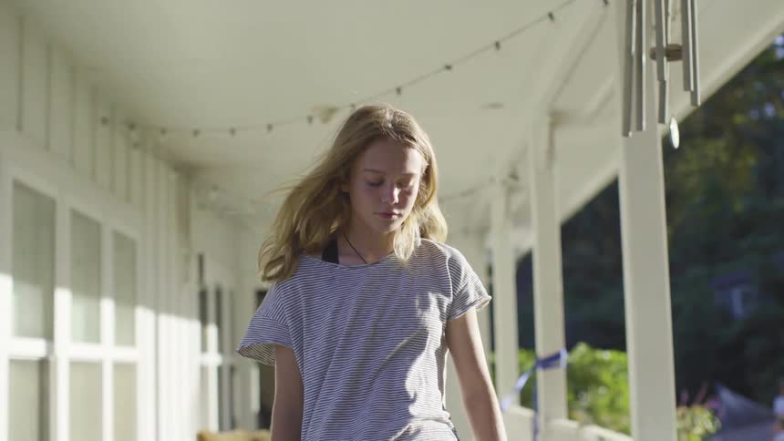 A girl stands on her porch on a windy day