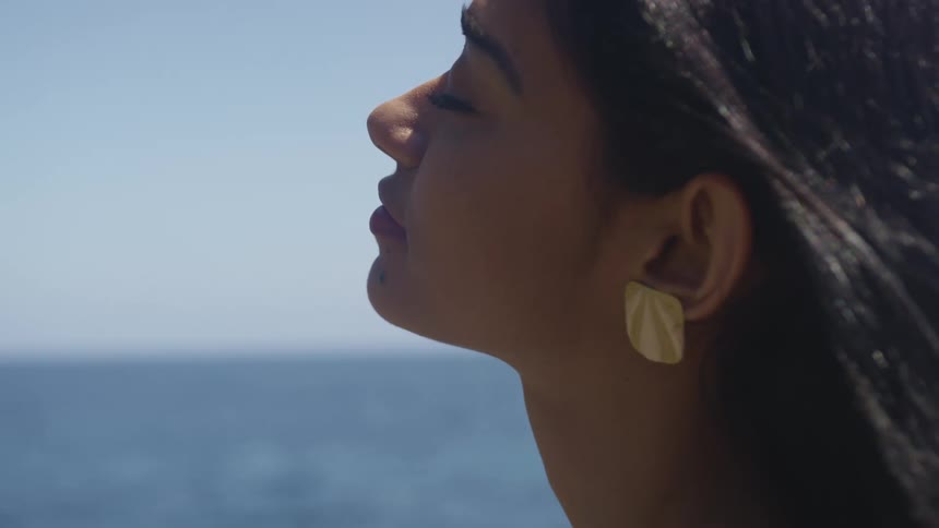 A woman holds he head upwards as she basks in the sunlight near the ocean