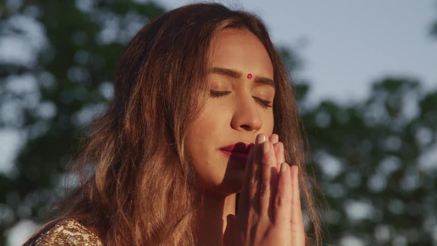 A woman is outdoors praying at dusk