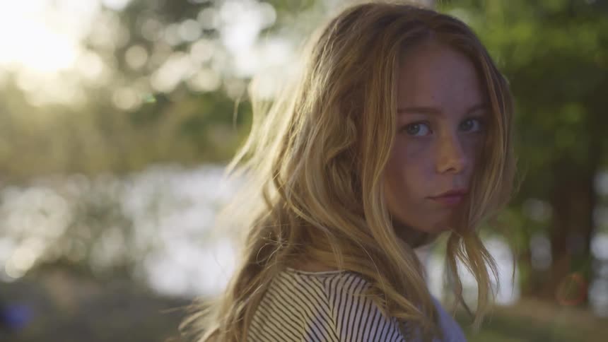 A young female looks directly at the camera while posing outdoors on a sunny day