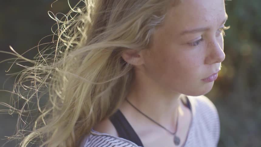 Young blonde girl looking at the horizon while the wind gently blows her hair at sunset