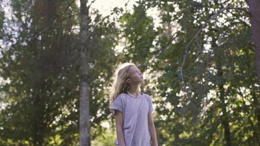 Little girl standing outside in a forest staring up at the sky at daytime