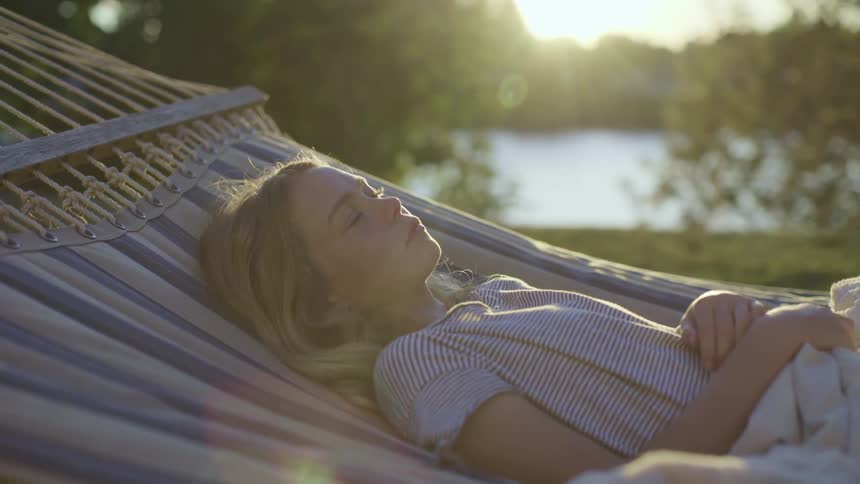 A man naps on a hammock outside by a lake