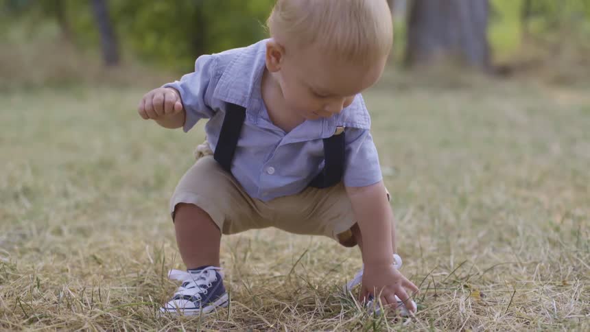 A cute little boy squats down to touch the grass beneath his feet