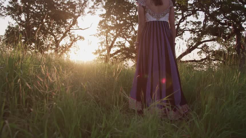 Woman wearing a dress walking over the tall grass at sunset