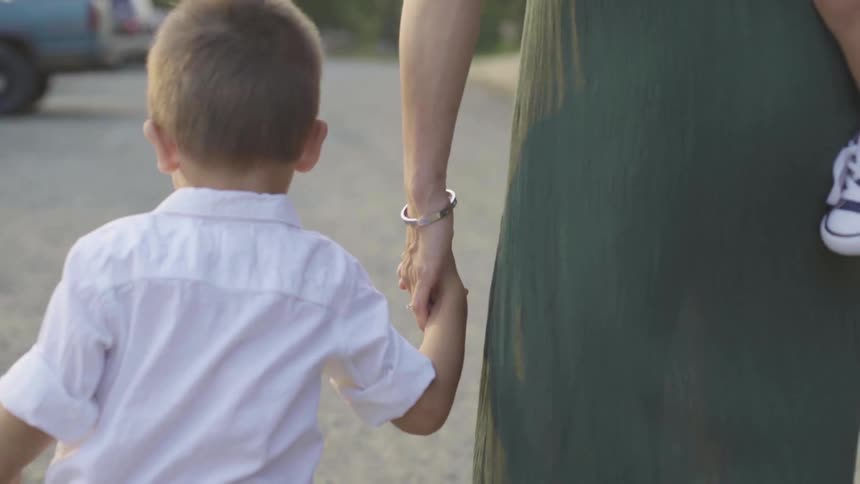 A woman walks through a parking lot while carrying her baby and holding her sons hand